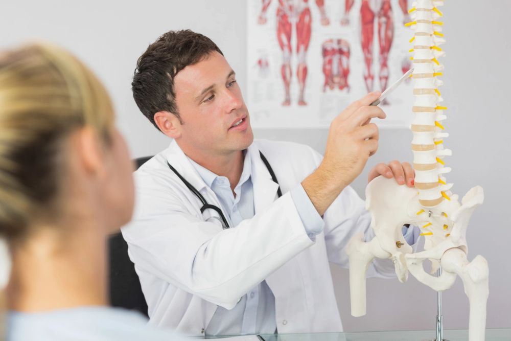 Doctor explaining spine anatomy using a skeletal model with a patient